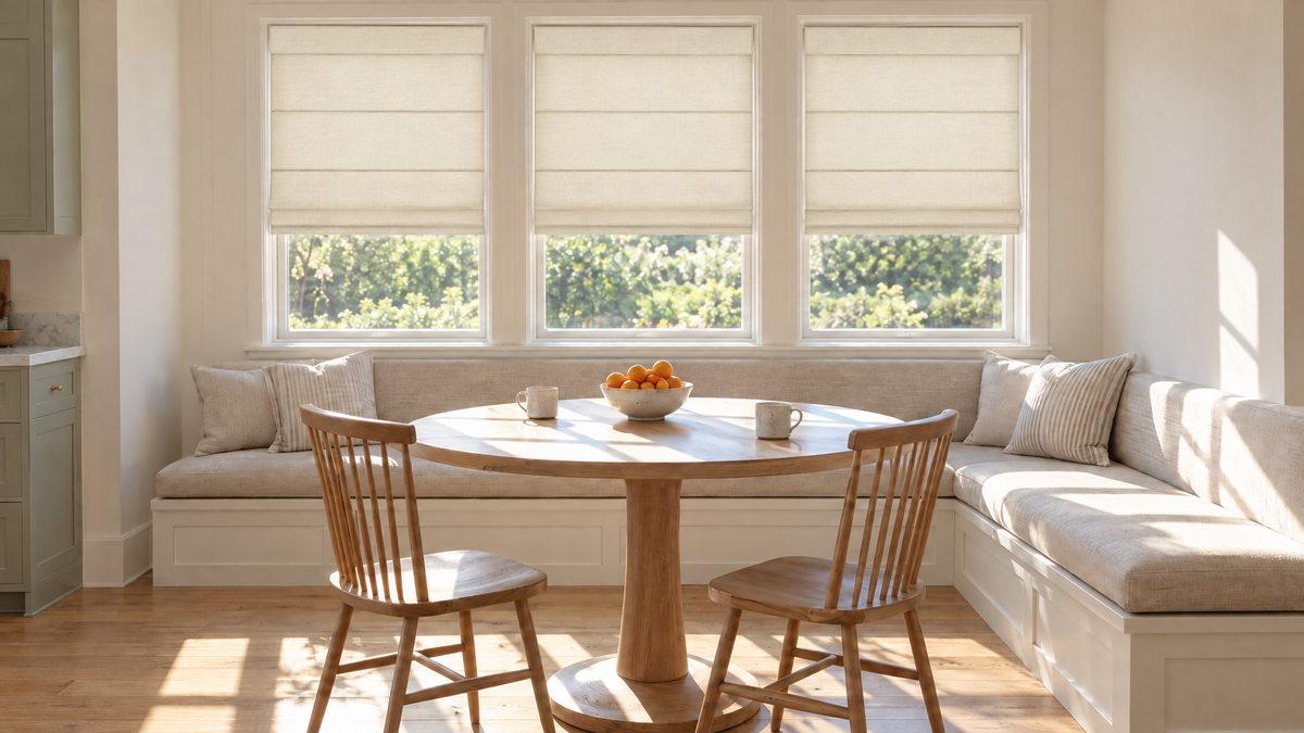 Light Filtering Roman Shades in Ivory — a breakfast nook in a lived-in family kitchen, early morning with bright directional sun