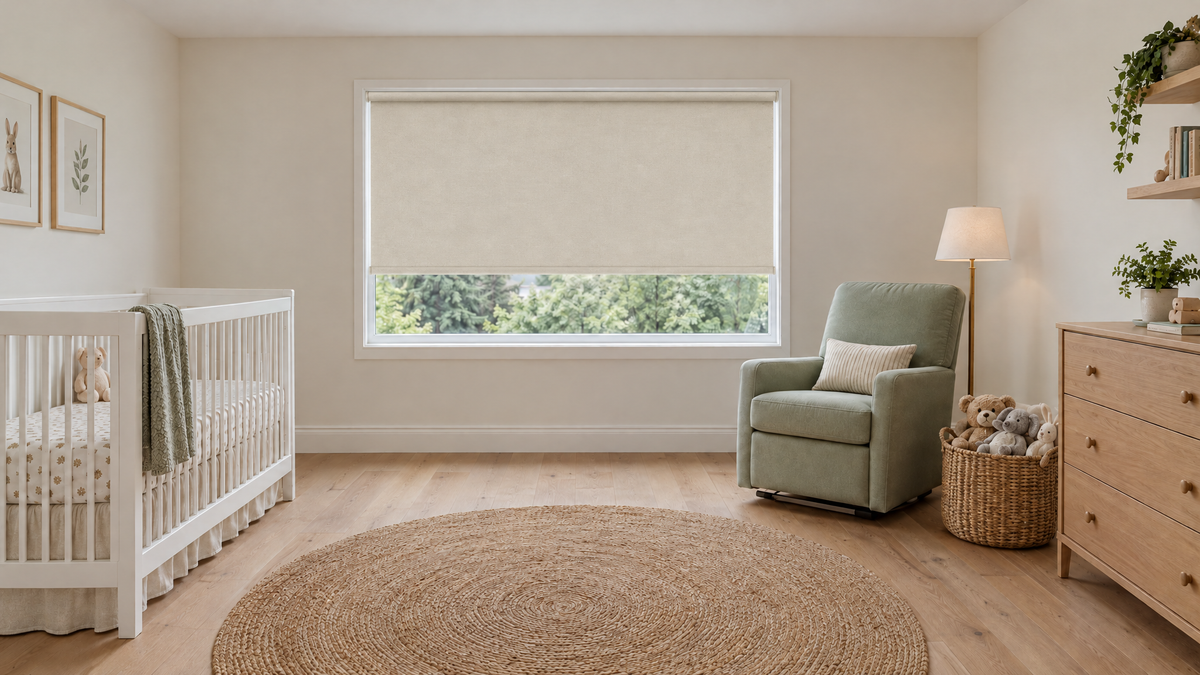 Blackout Roller Shades in Ivory — a calm nursery and toddler bedroom in a family home, fully furnished: a white wooden crib against the side wall, a soft sage green upholstered glider chair, a low natural wood dresser, a round jute rug, a basket of plush