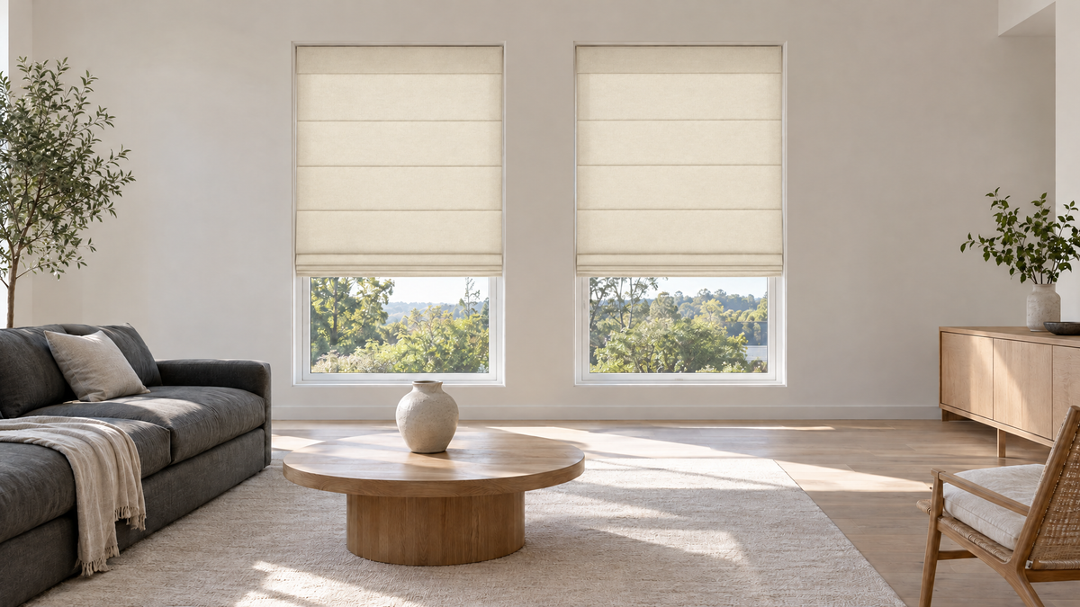 Light Filtering Roman Shades in Ivory — a modern living room in a recently built home, minimalist and fully furnished but uncluttered: a low charcoal linen sofa, a round white oak coffee table, a single large ceramic vase, a pale wool rug, smooth matte