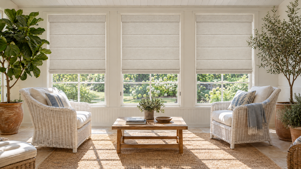 Light Filtering Roman Shades in Oatmeal — a designer sunroom addition on a traditional home, fully furnished in a relaxed coastal-meets-garden style: white painted wicker lounge chairs with linen cushions, a low teak coffee table, large potted