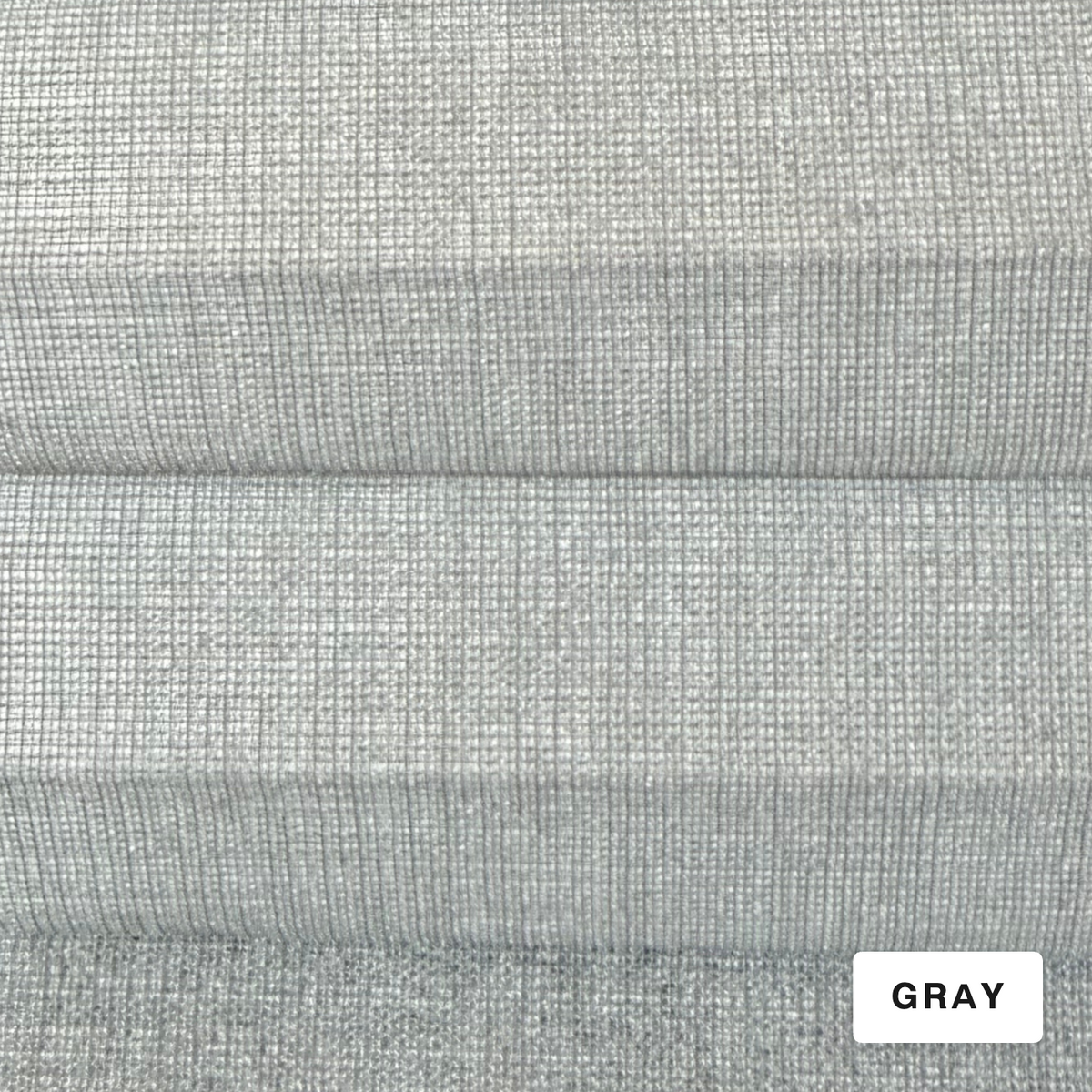 A close-up of a light gray woven fabric texture with horizontal folds and a small white label in the bottom right corner reading “GRAY.”.