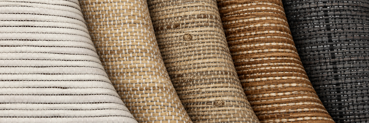 Close-up of several rolled fabric or material swatches in different colors and textures, including off-white, tan, brown, and dark charcoal, arranged side by side.